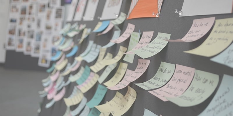 Dozens of sticky notes with writing on them, displayed on a board.